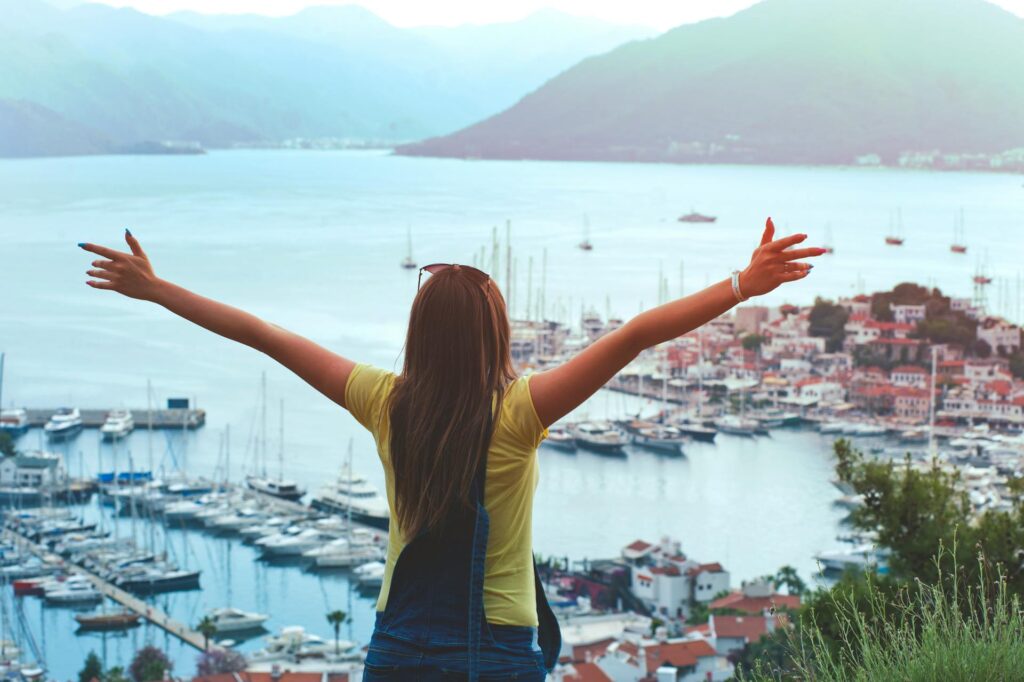 Woman raising her hands in the air looking out at a view of boats